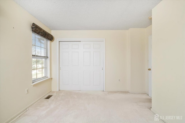 unfurnished bedroom with carpet flooring, a closet, visible vents, baseboards, and a textured ceiling