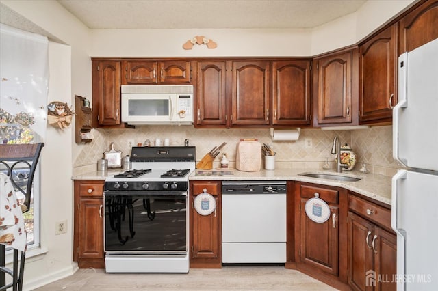 kitchen featuring tasteful backsplash, a sink, light stone countertops, light wood finished floors, and white appliances