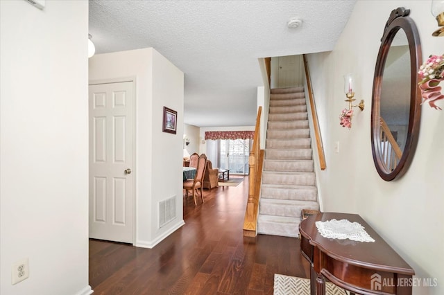 interior space featuring a textured ceiling, stairway, wood finished floors, and visible vents