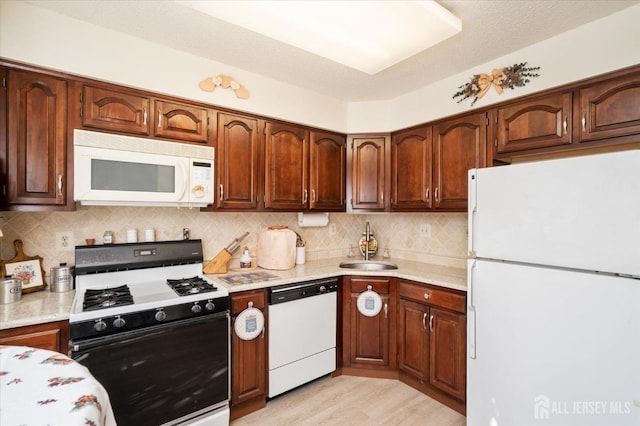 kitchen with a sink, white appliances, light wood-style flooring, and decorative backsplash