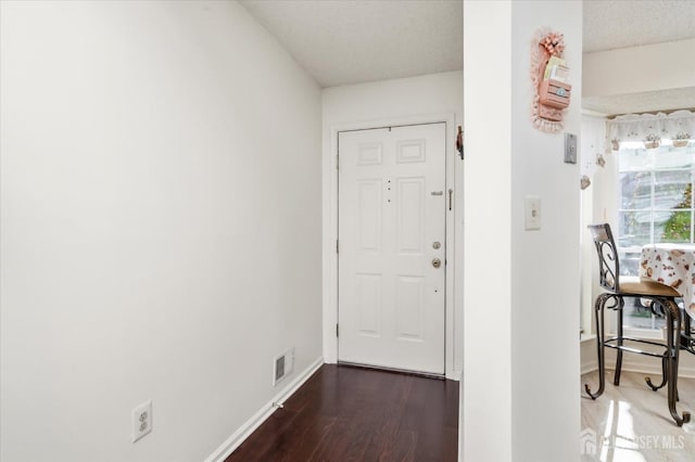 foyer with baseboards, visible vents, and wood finished floors
