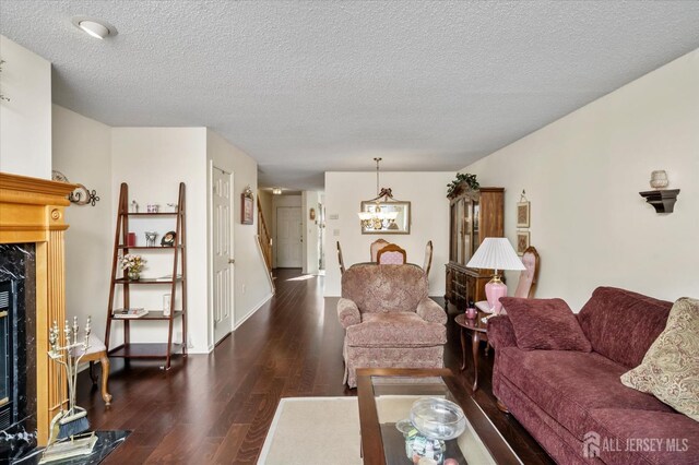 living room featuring a high end fireplace, a textured ceiling, dark wood-style flooring, and an inviting chandelier