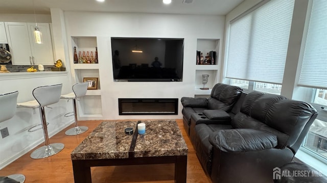 living area featuring built in shelves, a glass covered fireplace, and wood finished floors