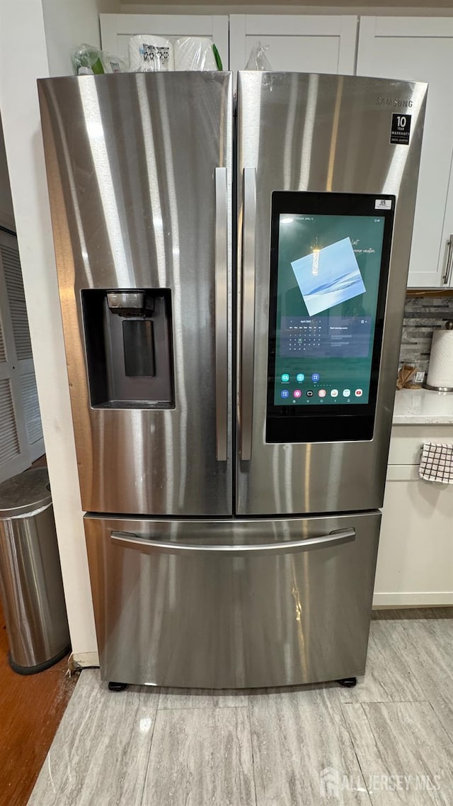 room details featuring white cabinetry, stainless steel fridge with ice dispenser, light countertops, and light wood-style floors