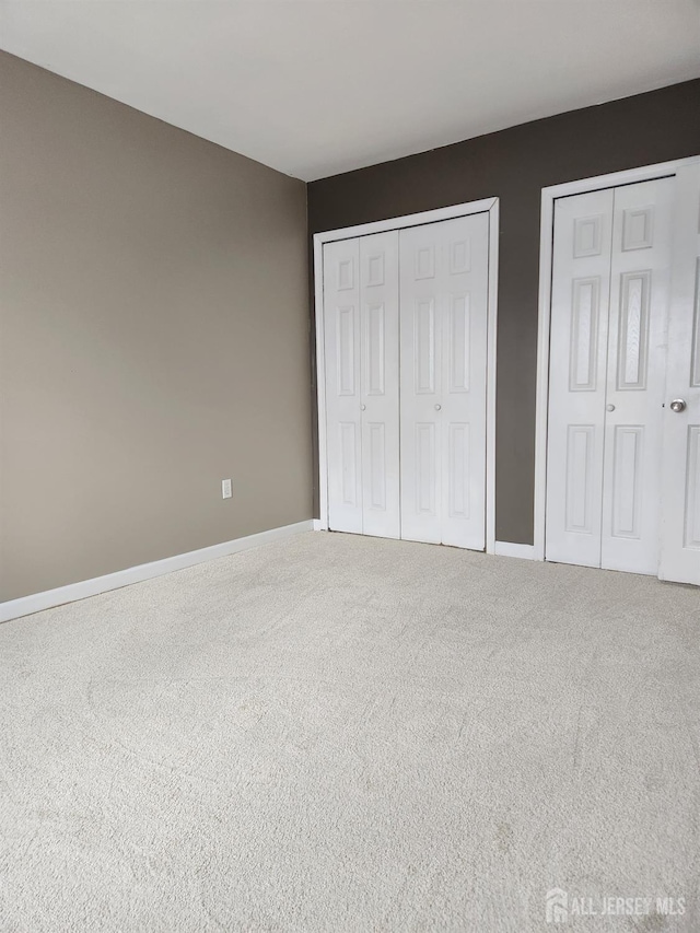 unfurnished bedroom featuring carpet, baseboards, and two closets