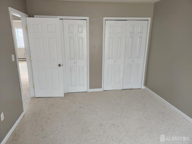 unfurnished bedroom featuring baseboards, carpet floors, a baseboard heating unit, and multiple closets