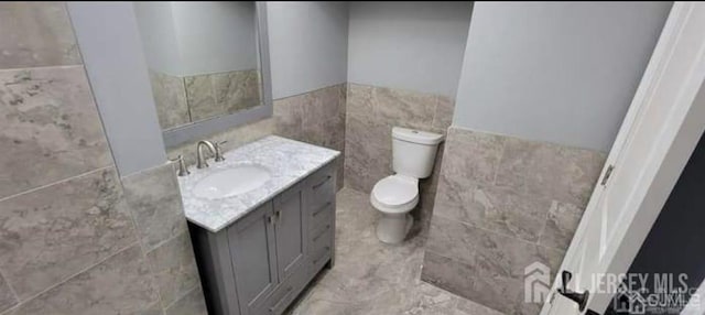 bathroom with tile walls, a wainscoted wall, vanity, and toilet