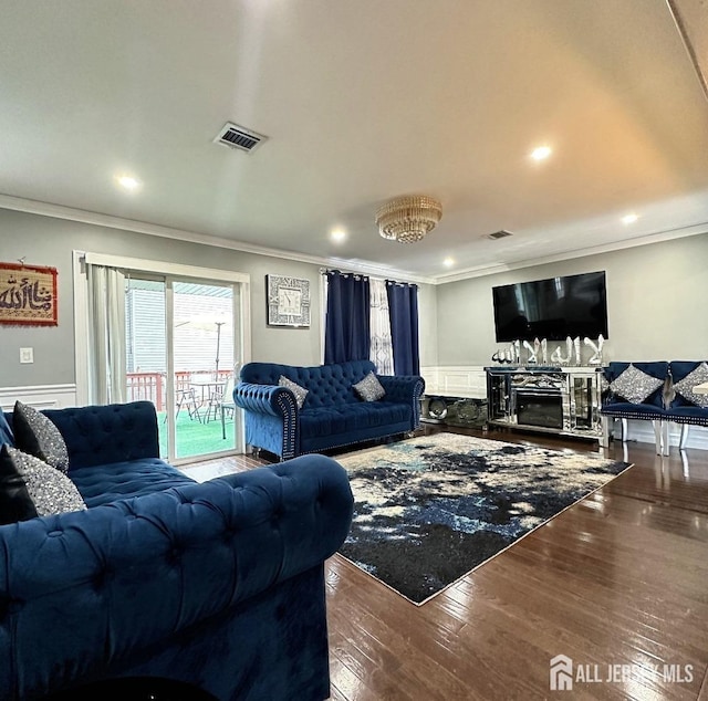 living room with crown molding, a glass covered fireplace, wood finished floors, and visible vents