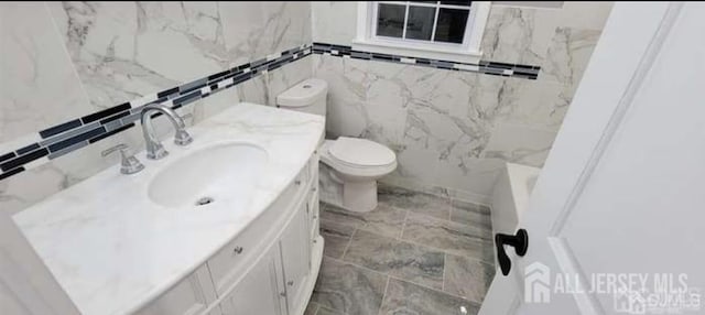 bathroom with toilet, tile walls, marble finish floor, and vanity