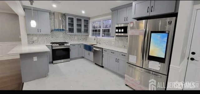 kitchen featuring wall chimney range hood, a sink, gray cabinets, stainless steel appliances, and a peninsula