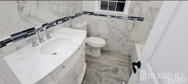 full bathroom with vanity, toilet, tile walls, and marble finish floor