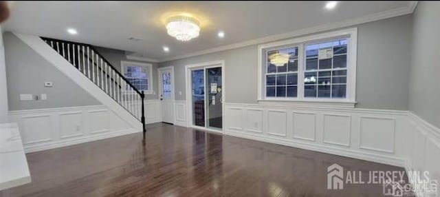 entrance foyer with wainscoting, a decorative wall, wood finished floors, ornamental molding, and stairway