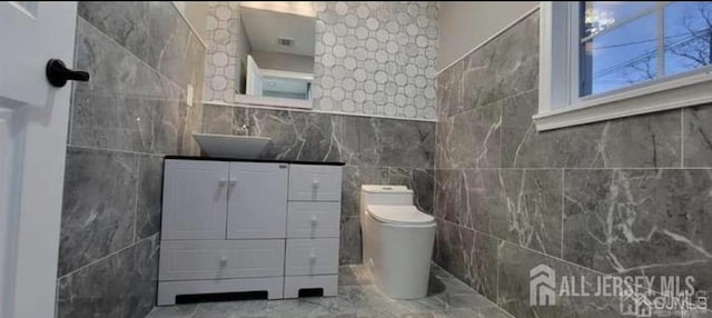 bathroom featuring vanity, marble finish floor, toilet, and tile walls