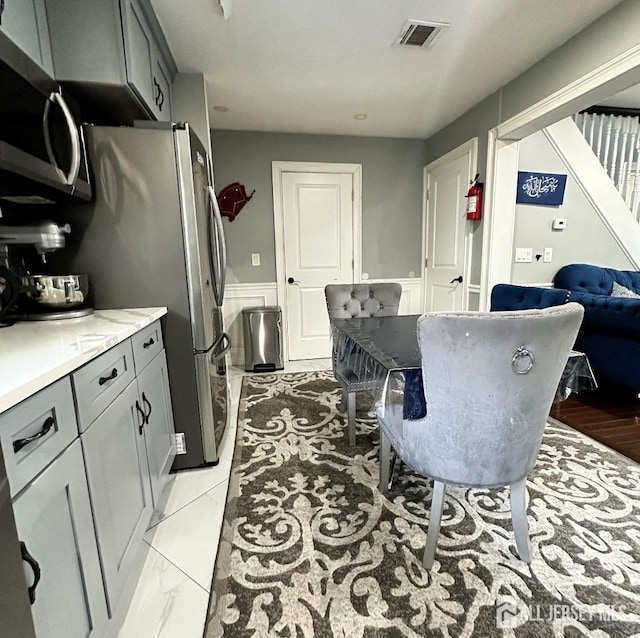 kitchen featuring a wainscoted wall, gray cabinets, stainless steel appliances, and visible vents
