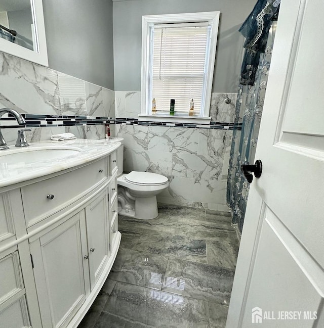 full bathroom featuring tile walls, wainscoting, vanity, toilet, and marble finish floor