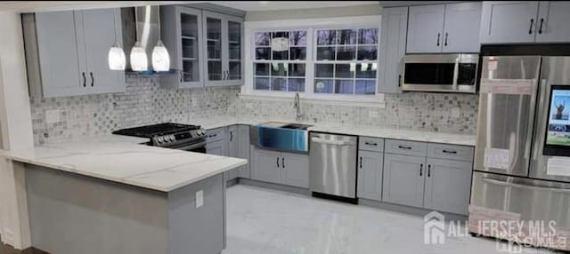 kitchen featuring wall chimney range hood, gray cabinetry, light stone counters, a sink, and stainless steel appliances