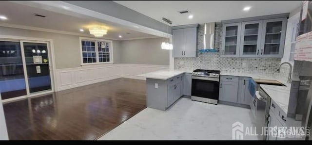 kitchen with wall chimney range hood, ornamental molding, gray cabinets, and gas range