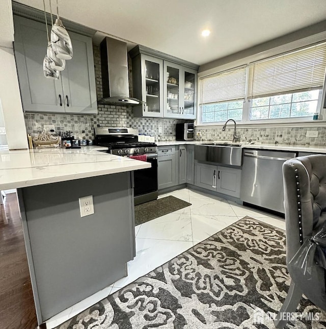 kitchen with wall chimney range hood, a sink, gray cabinets, stainless steel appliances, and a peninsula