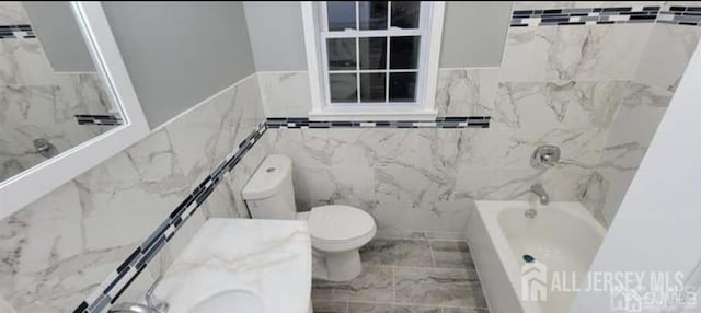 bathroom featuring tile walls, wainscoting, toilet, and tub / shower combination