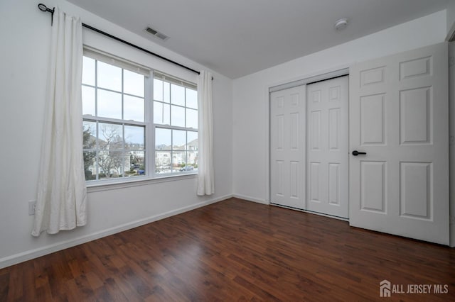 unfurnished bedroom with dark wood-style floors, visible vents, a closet, and baseboards