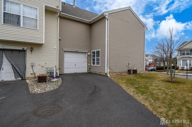 view of side of home with central AC unit, a garage, driveway, and a lawn