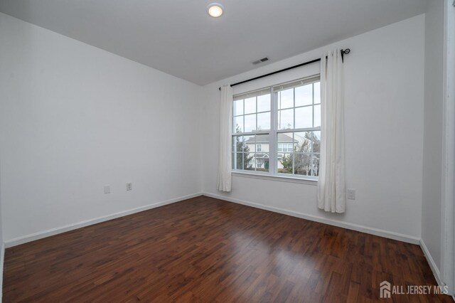 spare room with dark wood-style floors, visible vents, and baseboards