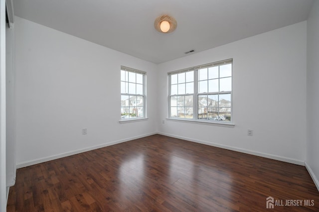 unfurnished room featuring visible vents, dark wood-type flooring, and baseboards