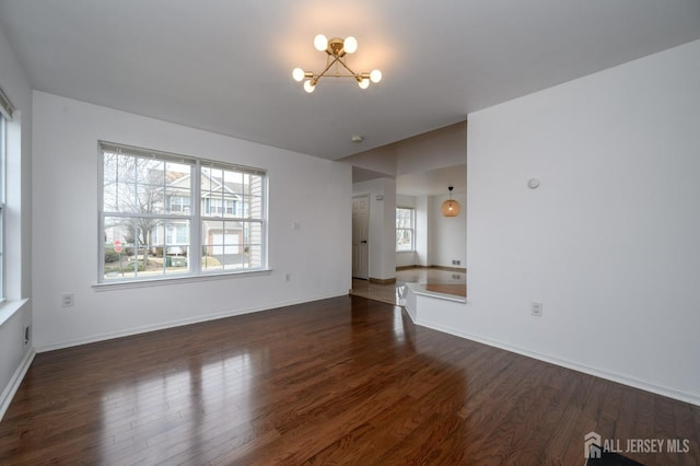 unfurnished living room featuring a chandelier, baseboards, and wood finished floors