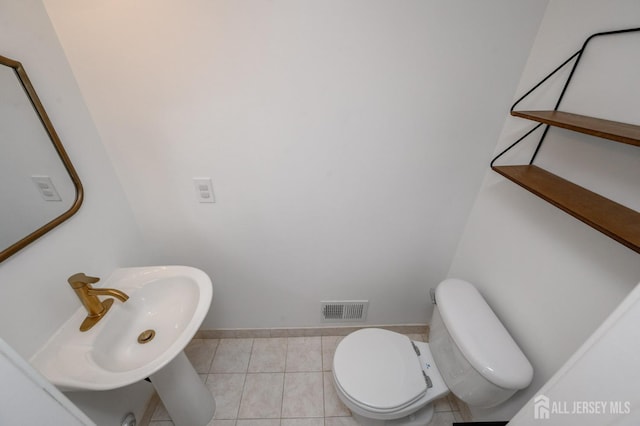 half bathroom with tile patterned floors, visible vents, toilet, a sink, and baseboards