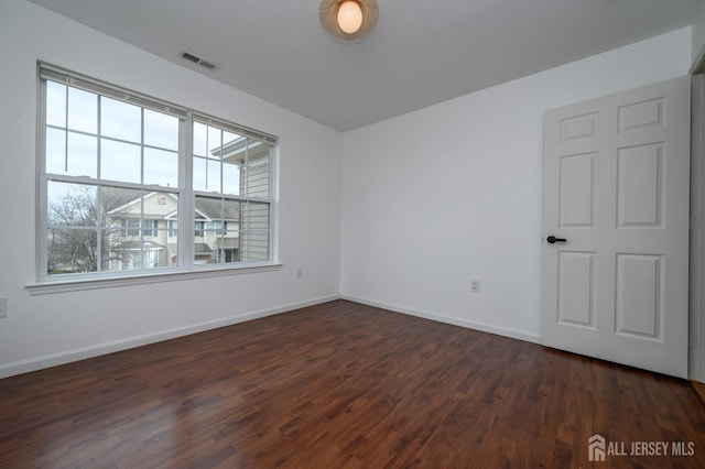 spare room featuring visible vents, baseboards, and dark wood finished floors