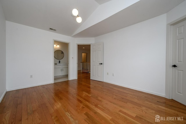 unfurnished bedroom featuring visible vents, lofted ceiling, a sink, light wood-style floors, and baseboards