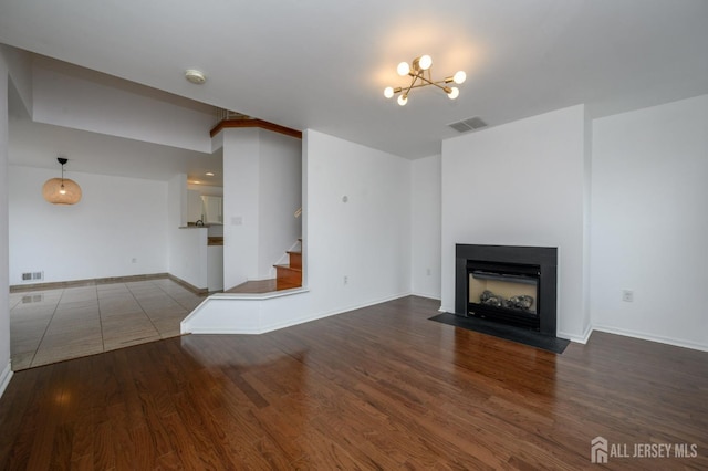 unfurnished living room with stairs, a fireplace with flush hearth, wood finished floors, and visible vents