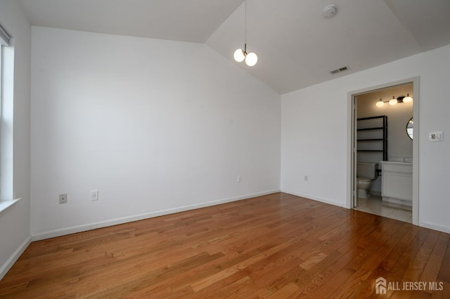 unfurnished room featuring lofted ceiling, baseboards, visible vents, and light wood-type flooring