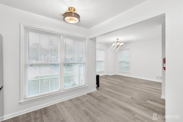 empty room with an inviting chandelier and light hardwood / wood-style flooring