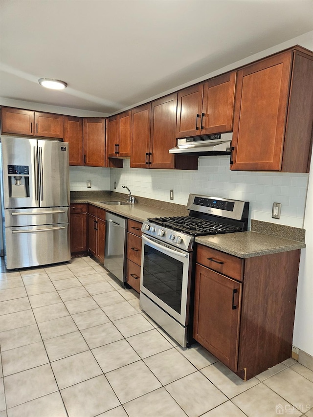 kitchen with under cabinet range hood, a sink, tasteful backsplash, dark countertops, and stainless steel appliances