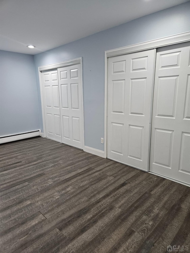 unfurnished bedroom featuring dark wood-style floors, baseboards, a baseboard radiator, recessed lighting, and multiple closets