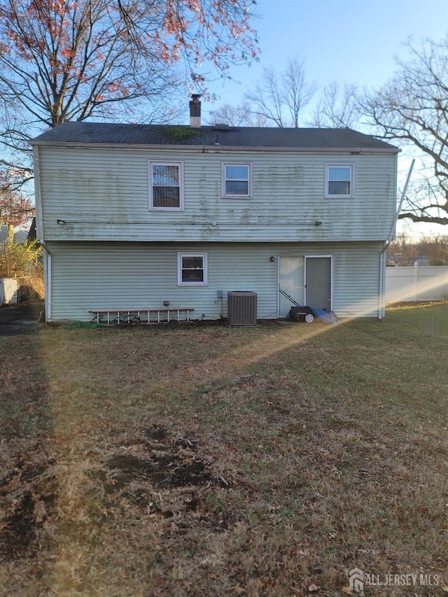 back of property featuring cooling unit, a lawn, a chimney, and fence