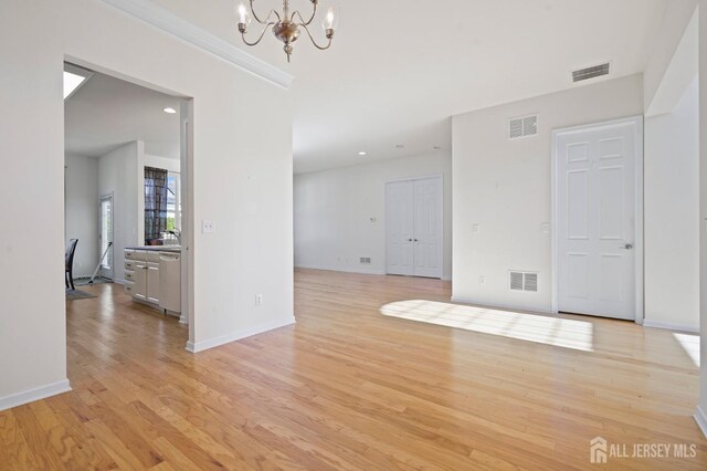 spare room with crown molding, an inviting chandelier, and light hardwood / wood-style flooring