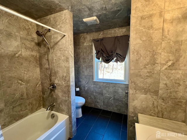 bathroom featuring tile patterned flooring, toilet, shower / bathing tub combination, and tile walls