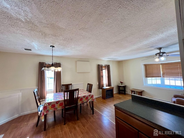 dining area featuring wood finished floors, a textured ceiling, ceiling fan, and a chandelier