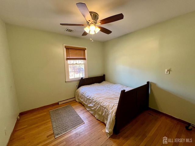 bedroom with a baseboard heating unit, wood finished floors, baseboards, and ceiling fan
