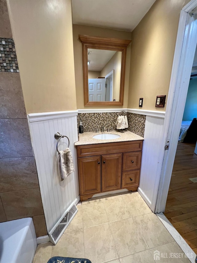 full bathroom featuring tile patterned flooring, visible vents, a wainscoted wall, a bathing tub, and vanity