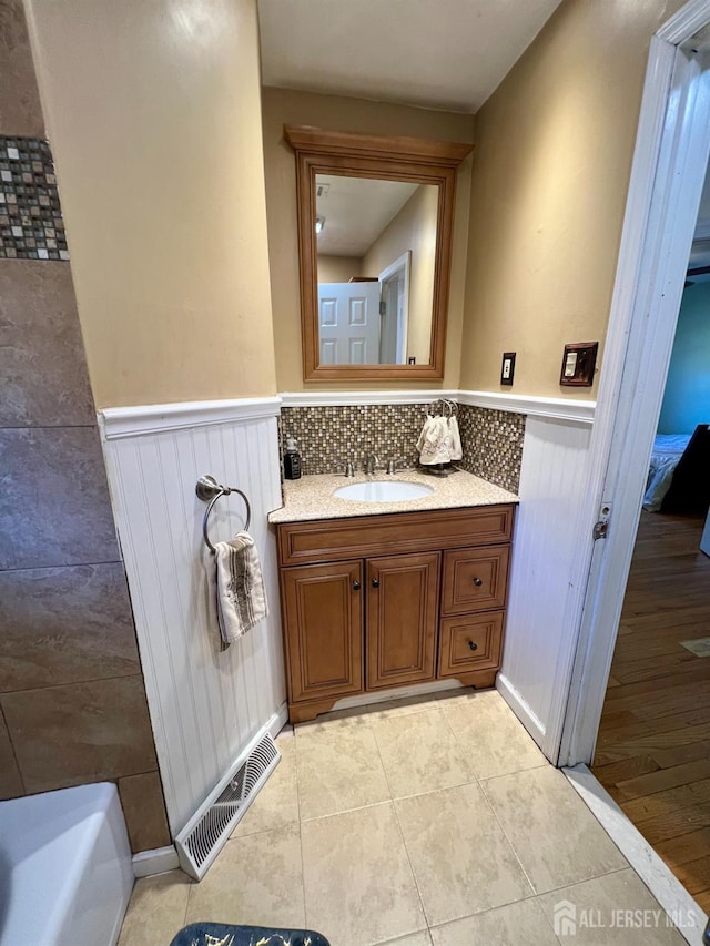 bathroom with a wainscoted wall, vanity, tile patterned flooring, and a bath