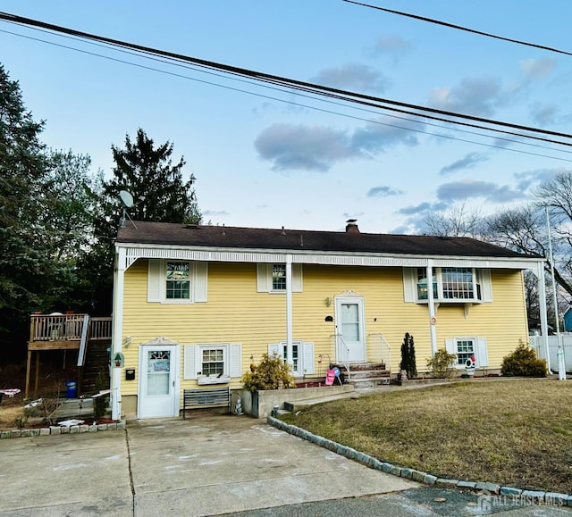 split foyer home with concrete driveway, a chimney, and a front lawn