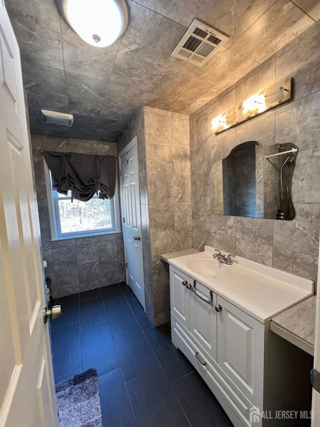 bathroom featuring visible vents, vanity, and tile walls