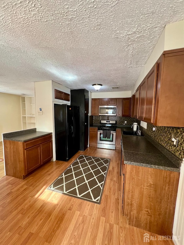 kitchen with light wood finished floors, stainless steel appliances, dark countertops, and a sink