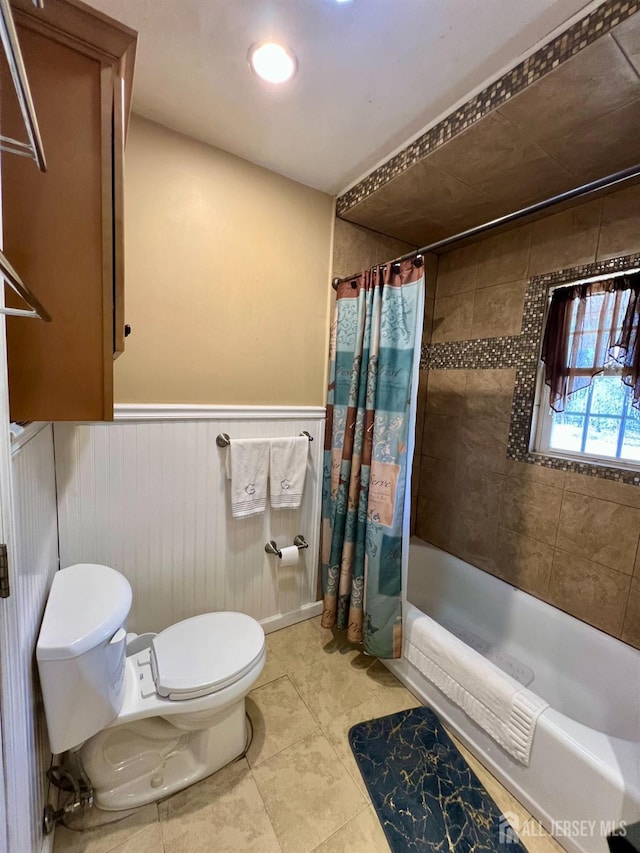 full bathroom with shower / bath combination with curtain, toilet, a wainscoted wall, and tile patterned floors