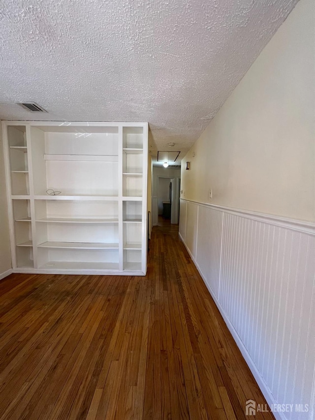 interior space with visible vents, a textured ceiling, hardwood / wood-style floors, and wainscoting