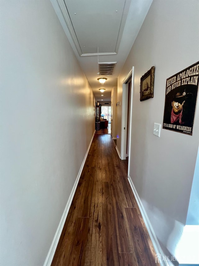 hall with attic access, dark wood-type flooring, and baseboards
