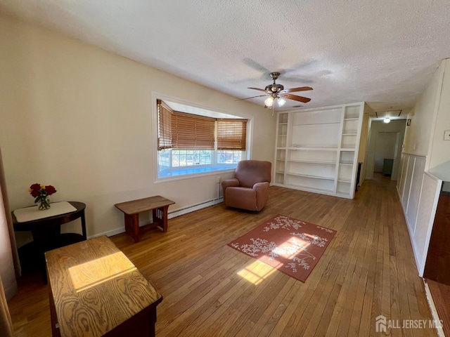 sitting room featuring baseboard heating, hardwood / wood-style flooring, a textured ceiling, built in shelves, and a ceiling fan